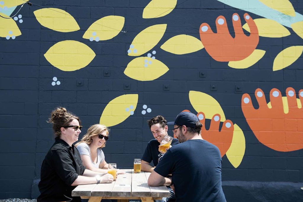 Belleflower Brewery owners enjoy pints of beer in the urban beer garden beneath a whimsical mural.