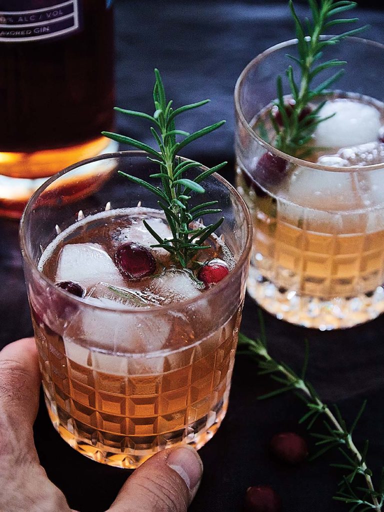 Making cocktails at home with cranberry gin from Sweetgrass Winery and Distillery and ginger ale, garnished with a rosemary sprig and fresh Maine cranberries.